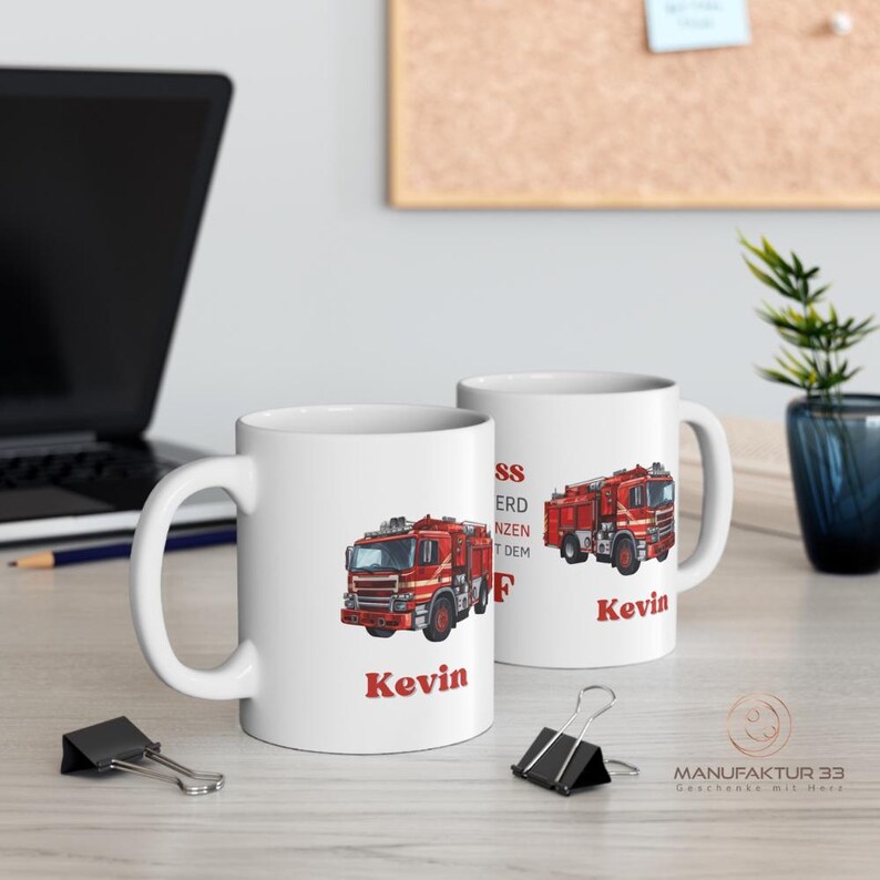 May include: Two white ceramic mugs with a red fire truck design and the name "Kevin" in red. One mug shows the fire truck on the front, and the other shows the fire truck on the side. The mugs are on a light-colored surface.