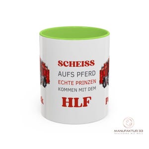 May include: White ceramic mug with a green interior and a red fire truck graphic. The mug features red text that reads "SCHEISS AUFS PFERD ECHTE PRINZEN KOMMEN MIT DEM HLF". The mug has a glossy finish.