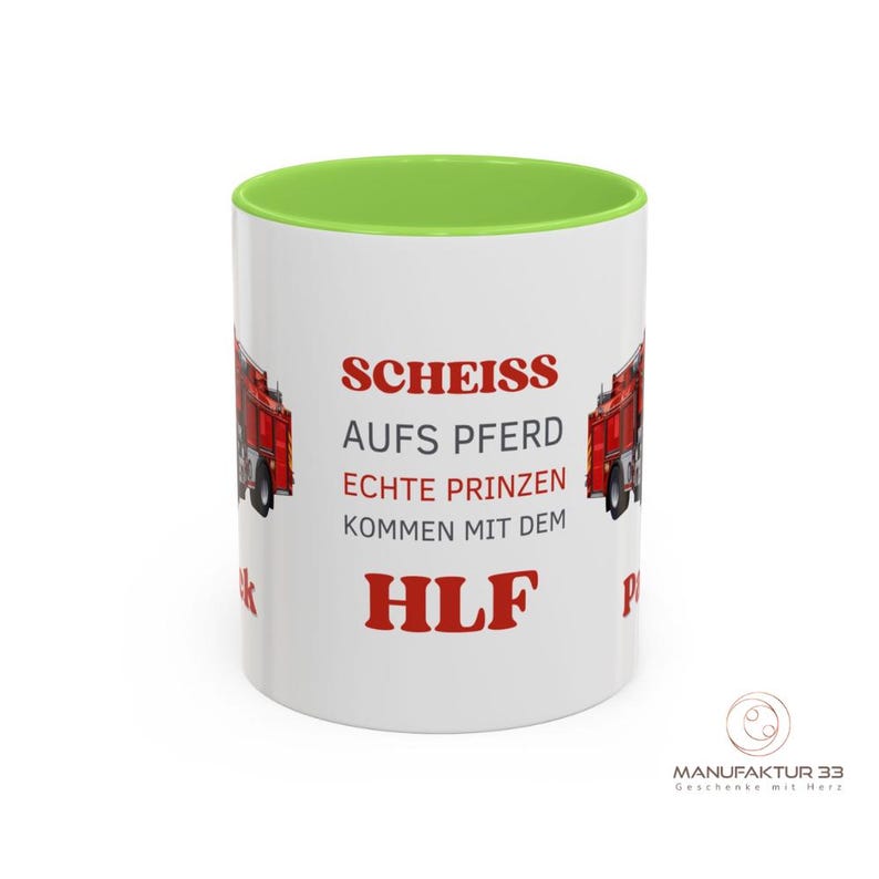 May include: White ceramic mug with a green interior and a red fire truck graphic. The mug features red text that reads "SCHEISS AUFS PFERD ECHTE PRINZEN KOMMEN MIT DEM HLF". The mug has a glossy finish.