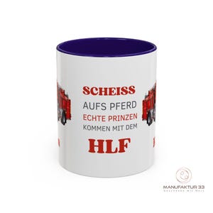 May include: White ceramic mug with a navy blue interior and a red and white design. The mug features a red fire truck graphic and German text. The text includes the word "HLF" in red. The mug has a glossy finish.