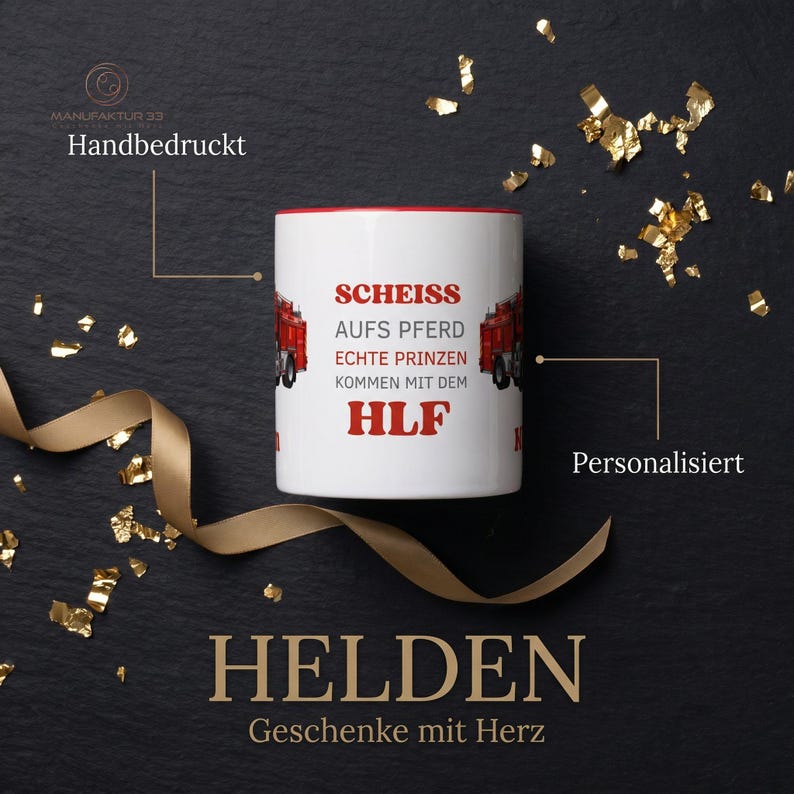 May include: White ceramic mug with a red interior and a design featuring red fire trucks and German text. The mug has the text "SCHEISS AUFS PFERD ECHTE PRINZEN KOMMEN MIT DEM HLF". Gold confetti and a ribbon are in the background.