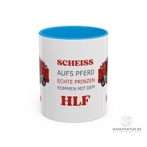 May include: White ceramic mug with a blue interior and a red fire truck graphic. The mug features red text that reads "SCHEISS AUFS PFERD ECHTE PRINZEN KOMMEN MIT DEM HLF". The mug has a glossy finish.