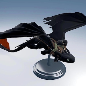 Puede incluir: Figura de dragón negro con grandes alas y un detalle de aleta naranja. Una persona está montada en la espalda del dragón. La figura está montada sobre una base circular transparente, sobre un fondo azul claro.