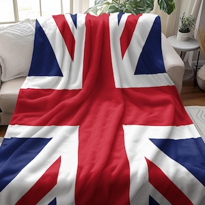 Pode incluir: Um cobertor macio com a bandeira britânica, a Union Jack, sobre um sofá. O design apresenta as cores vermelha, branca e azul da bandeira. A textura do cobertor sugere conforto e calor.