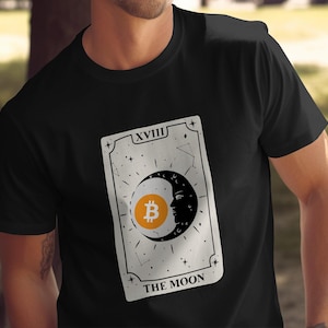 May include: Black t-shirt featuring a tarot card design. The card depicts a crescent moon with a face, a Bitcoin symbol, and the words "THE MOON". The card is framed with stars and the Roman numeral XVIII.