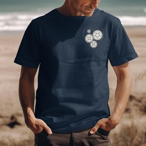 May include: Navy blue t-shirt featuring a heart-shaped design composed of gears. The gears are in a light cream color, creating a contrast against the dark blue fabric. The shirt is a classic crew neck style.