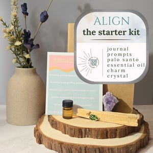 May include: An "Align the Starter Kit" with a journal, prompts, palo santo, essential oil, charm, and crystal. The kit is arranged on a wooden slice, with a vase of flowers to the left. The kit includes a small bottle of essential oil.