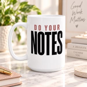 May include: A white ceramic mug with a handle on the left side. The front of the mug features the text DO YOUR in a muted rose color, positioned above the word NOTES in large, bold black capital letters. The mug has a smooth, glossy finish.