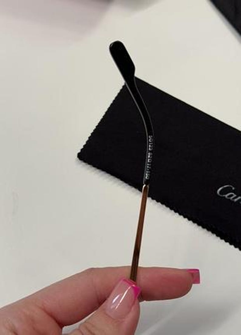 May include: A gold metal eyeglass arm with a black plastic tip. The arm is engraved with the text 'Made in Italy'.
