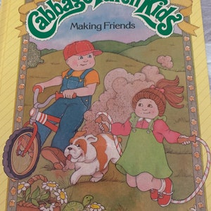 Op de afbeelding: Een boekomslag met een groene en gele illustratie van het Cabbage Patch Kids-logo met de tekst "Making Friends". De omslag toont ook een kleurrijke illustratie van twee Cabbage Patch Kids-poppen, een rijdt op een fiets en de andere springt touwtje met een rood en wit touw. Het boek is getiteld "A Parker Brothers Story Book" met de tekst "Story by Kathleen N. Daly Pictures by Maryann Cocca-Leffler".
