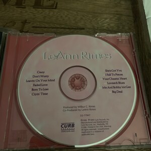 May include: A pink CD with a red border featuring a photo of country music singer LeAnn Rimes. The CD title is "LeAnn Rimes" and the track list is printed on the CD. The CD is labeled "Curb Records" and includes copyright information.