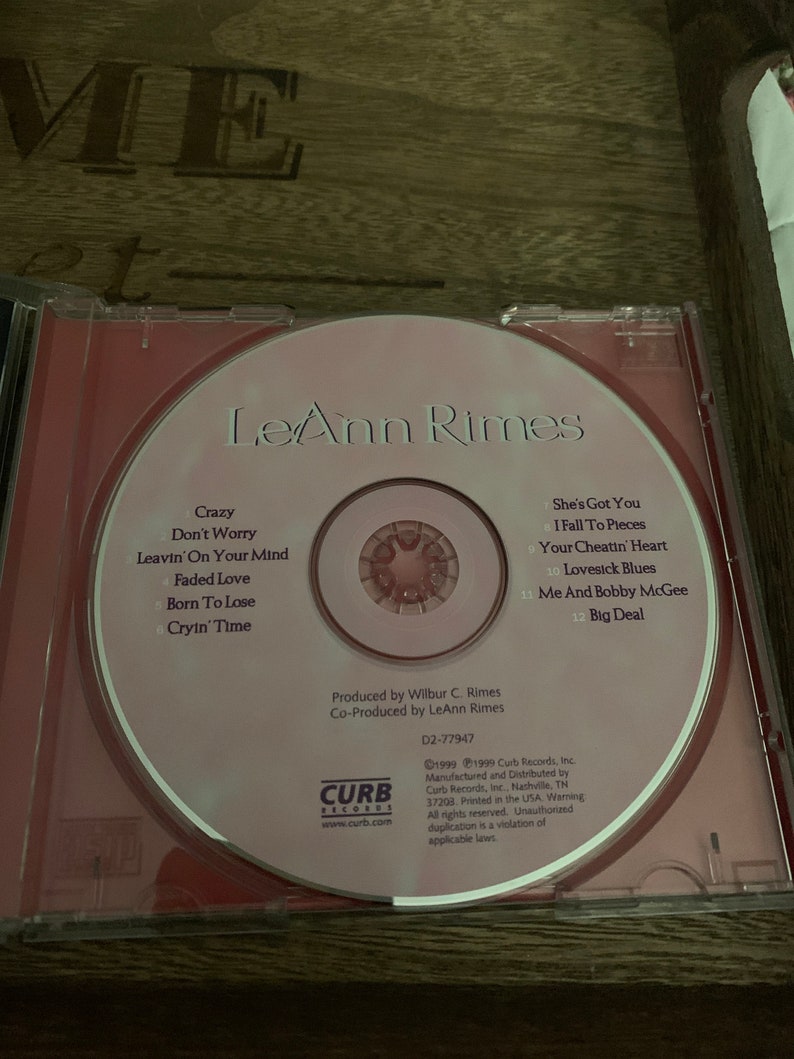 May include: A pink CD with a red border featuring a photo of country music singer LeAnn Rimes. The CD title is "LeAnn Rimes" and the track list is printed on the CD. The CD is labeled "Curb Records" and includes copyright information.