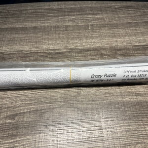 May include: A rolled-up paper puzzle with a black and white design. The label reads "Crazy Puzzle # 576-11" and "Different Strokes P.O. Box 15218 Rio Rancho, NM 87174".