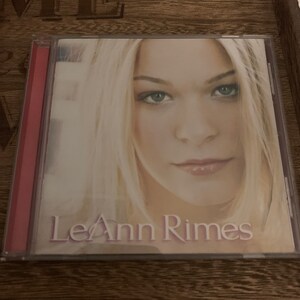 Op de afbeelding: Een CD-hoes met een foto van LeAnn Rimes op de voorkant. De hoes is van doorzichtig plastic met een rode rug. De foto toont LeAnn Rimes met blond haar tegen een lichte achtergrond.