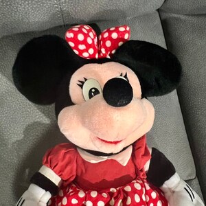 K&ouml;nnte beinhalten: Ein Pl&uuml;schtier von Minnie Mouse, das ein rotes Kleid mit wei&szlig;en Punkten und eine rote Schleife mit wei&szlig;en Punkten tr&auml;gt.