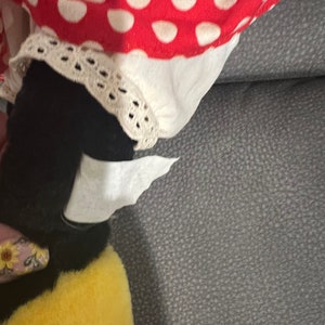 K&ouml;nnte beinhalten: Ein schwarzes und gelbes Pl&uuml;schtier in Form einer Biene mit einem wei&szlig;en und rot gepunkteten Kleid auf einem grauen Sofa.