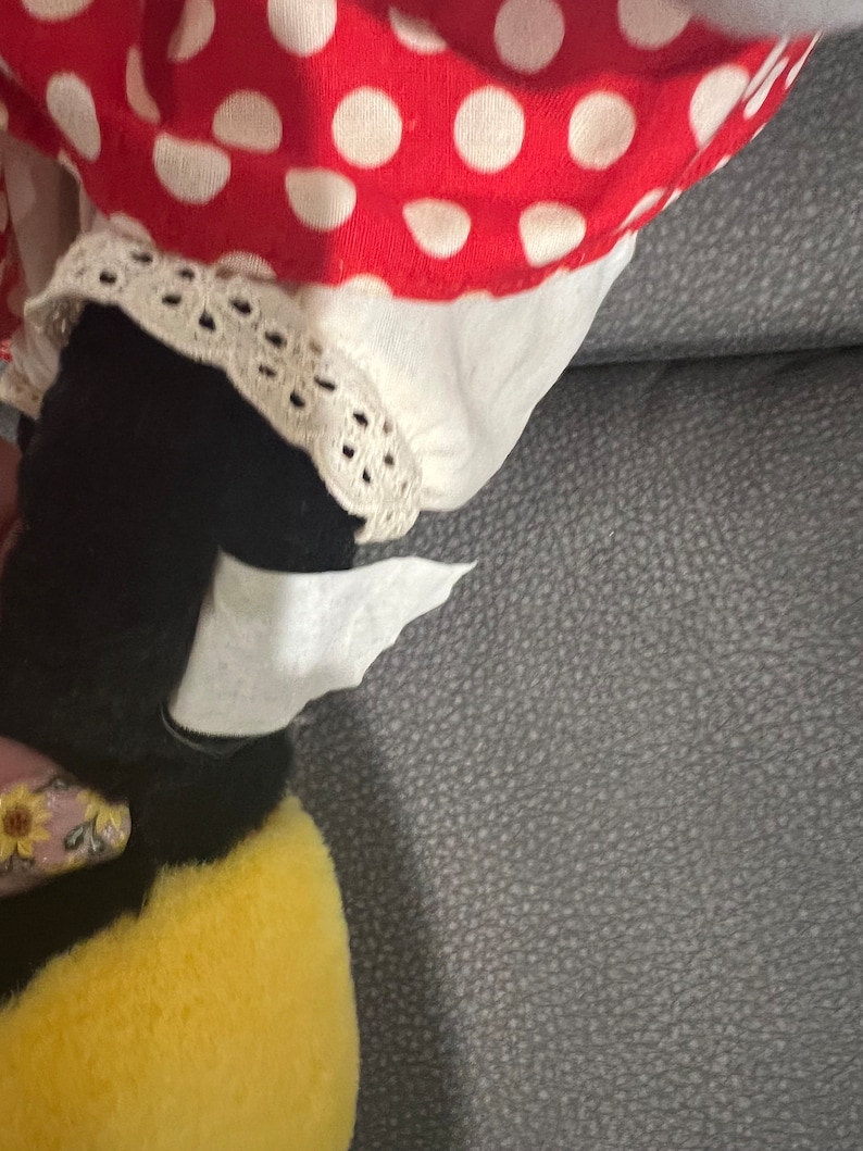 K&ouml;nnte beinhalten: Ein schwarzes und gelbes Pl&uuml;schtier in Form einer Biene mit einem wei&szlig;en und rot gepunkteten Kleid auf einem grauen Sofa.