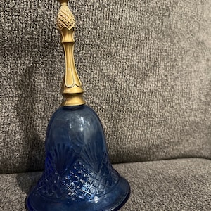 Op de afbeelding: Een blauwe glazen bel met een goudkleurige metalen bovenkant. De bel heeft een ruitvormig patroon.