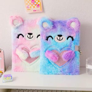Könnte beinhalten: Zwei flauschige, farbenfrohe Bären-Tagebücher. Eines ist rosa und das andere blau und lila. Jedes Tagebuch hat ein herzförmiges Design mit Schloss und Schlüssel. Die Tagebücher haben Bärenohren und ein lächelndes Gesicht.
