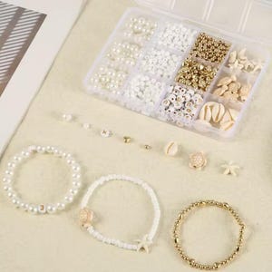 May include: A clear plastic organizer filled with various beads, including pearls, white, and gold beads, along with small seashell and turtle charms. Three bracelets are displayed, one with pearls and the number "3", and two others with white and gold beads.
