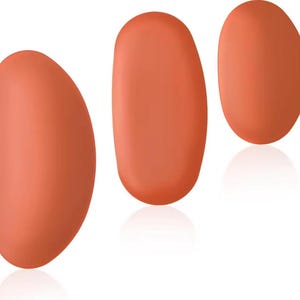 Puede incluir: Tres objetos lisos de forma ovalada, en un cálido color coral, se disponen sobre un fondo blanco. Los objetos tienen una forma redondeada y orgánica, con un sutil degradado que sugiere un acabado suave y mate. La disposición crea movimiento.