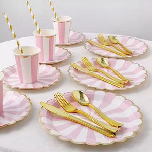 Può includere: Una tavola per feste con bicchieri, piatti e posate dorate a righe rosa e bianche. I piatti hanno un bordo smerlato. Nelle tazze ci sono cannucce di carta a righe oro e bianco.