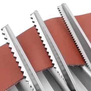 Peut inclure: Gros plan sur trois outils métalliques aux bords dentelés, inclinés contre une surface brun rougeâtre. Les outils semblent être en acier inoxydable, avec des dents tranchantes et régulièrement espacées le long de leurs bords.