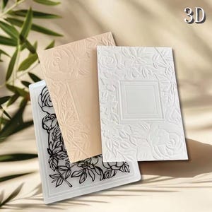 May include: Three rectangular embossing folders featuring floral rose patterns. One folder is clear with black outlines, one is light peach, and one is white. Each folder displays a central rectangular frame surrounded by embossed roses and leaves.