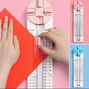 Puede incluir: Un cortador de papel rosa y blanco con una regla transparente y una parte superior circular rosa. El cortador está cortando un trozo de papel rojo. También se muestran cortadores adicionales con tapas azules y rosas.
