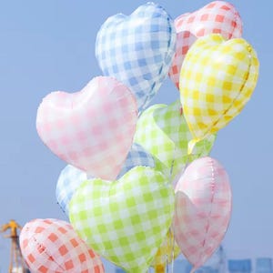 May include: A cluster of heart-shaped balloons in various colors, including pink, yellow, blue, and green. Each balloon features a gingham pattern. The balloons are against a clear, light blue sky.