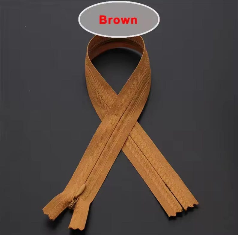 Puede incluir: Cremallera marr&oacute;n con tirador a juego, dispuesta en un patr&oacute;n decorativo. La palabra "Brown" se muestra en un &oacute;valo blanco encima de la cremallera. Los dientes de la cremallera son visibles.