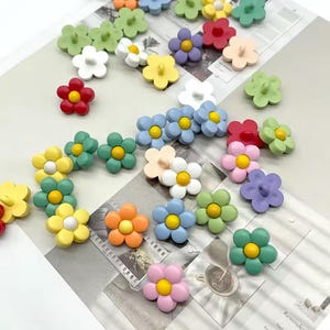 Puede incluir: Una colección de botones coloridos con forma de flor en varios tonos, incluyendo rojo, amarillo, azul, verde y rosa. Cada botón tiene un centro contrastante, creando una estética alegre y juguetona. Estos botones decorativos son ideales para proyectos de manualidades.