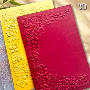 Op de afbeelding: Close-up van drie reliëfkaarten in geel, rood en lichtblauw. De kaarten hebben een bloemenontwerp langs de randen. De rode kaart heeft de tekst "3D" in de rechterbovenhoek. De kaarten hebben een getextureerd oppervlak.