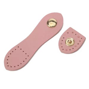Può includere: Due chiusure per borse in pelle rosa con bottoni automatici color oro. Una chiusura è allungata con fori preforati per cucire, l'altra è un pezzo più piccolo e arrotondato con un bottone automatico.