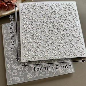 Puede incluir: Dos carpetas de relieve cuadradas y transparentes, cada una de 15 cm (5,9 pulgadas) de lado. Las carpetas presentan un patrón repetitivo de huellas de patas. Estas carpetas están diseñadas para manualidades y crear diseños texturizados.