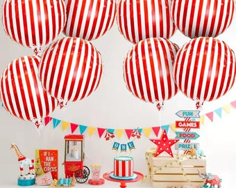 May include: A festive circus-themed party scene with red and white striped balloons, a small cake, and a popcorn machine. Colorful bunting and a star-shaped decoration add to the celebratory atmosphere. The scene includes a giraffe figurine and a sign that reads "If I Ran the Circus."