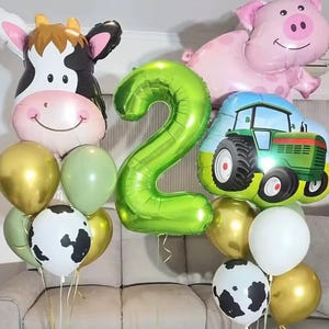 Könnte beinhalten: Ballonsammlung zum Thema Bauernhof, darunter eine Kuh, ein Schwein und ein Traktor, zusammen mit grünen und goldenen Ballons. Ein großer grüner Ballon mit der Zahl 2 deutet auf einen zweiten Geburtstag hin.
