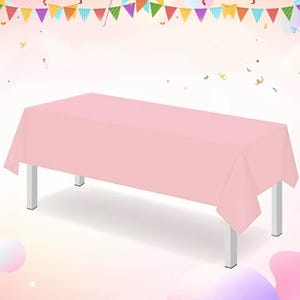 May include: A light pink rectangular tablecloth draped over a white-legged table. The tablecloth is smooth and covers the entire table surface. Colorful pennant banners hang in the background, suggesting a festive occasion.