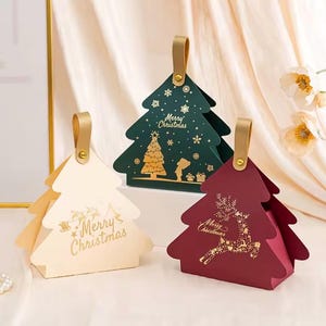 May include: Three Christmas tree-shaped gift boxes with gold handles. The cream box features a gold sleigh design, the green box shows a gold tree and snowflake pattern, and the maroon box displays a gold reindeer, all with Merry Christmas text.
