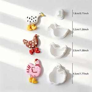 Può includere: Una collezione di formine per biscotti e figurine decorative a tema animali della fattoria. Le figurine includono un'anatra bianca con macchie nere, una gallina marrone con stivali rossi e una gallina rosa con stivali gialli. Le formine misurano fino a 4,5 cm.
