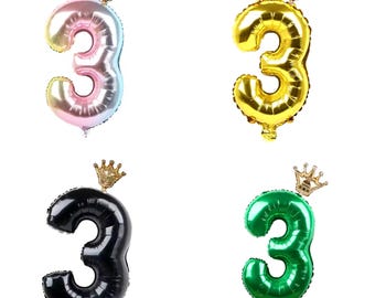 Pode incluir: Quatro balões de número três de folha de ouro com coroas douradas. Os balões são rosa, dourado, preto e verde.