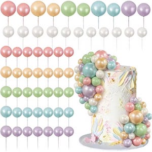 Peut inclure: Une collection de décorations de gâteaux en forme de perles de différentes couleurs pastel, dont rose, pêche, vert, bleu et lavande. Certaines décorations sont disposées sur un gâteau, d'autres sont présentées individuellement. Le gâteau est blanc avec des accents colorés.