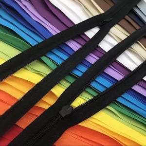 Puede incluir: Primer plano de cremalleras de colores, dispuestas en un arco&iacute;ris. Las cremalleras tienen cintas y tiradores negros. La imagen est&aacute; bien iluminada, revelando los detalles de los dientes de la cremallera. Ideal para costura y proyectos creativos.