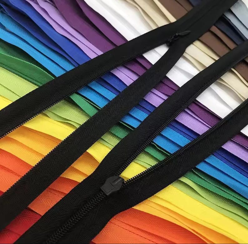 Puede incluir: Primer plano de cremalleras de colores, dispuestas en un arco&iacute;ris. Las cremalleras tienen cintas y tiradores negros. La imagen est&aacute; bien iluminada, revelando los detalles de los dientes de la cremallera. Ideal para costura y proyectos creativos.