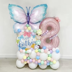 Könnte beinhalten: Eine farbenfrohe Geburtstagsballon-Anordnung mit einem großen Schmetterling, der Zahl acht und einem "Happy Birthday"-Ballon. Die Ballons sind in Pastellfarben wie Rosa, Blau und Gelb gehalten und schaffen eine festliche Atmosphäre.