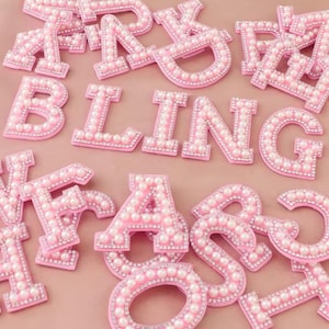 Può includere: Lettere in feltro rosa con decorazioni di perle, che compongono la parola "BLING".