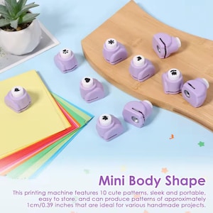 Könnte beinhalten: Eine Sammlung kleiner, lila Mini-Körper-Form-Papierstanzer mit verschiedenen Musterdesigns. Das Bild zeigt auch farbiges Papier und eine kleine Topfpflanze. Der Text lautet "Mini Body Shape" und beschreibt die Stanzer als Muster mit 1 cm.