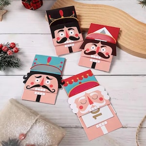 May include: Four rectangular paper cards featuring colorful nutcracker illustrations. Each card displays a distinct character with a mustache, painted teeth, and a unique hat. One card shows a closed mouth, while another reveals a gold number 10.