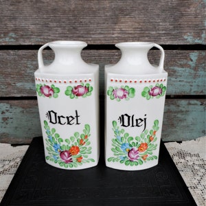 May include: Two white ceramic oil and vinegar cruets with floral designs and the words "Ocet" and "Olej" painted on them.