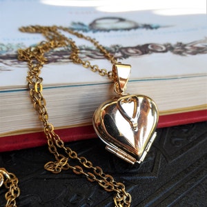 May include: A gold heart-shaped locket necklace with a chain. The locket has a hinged opening and a small heart-shaped design on the front.